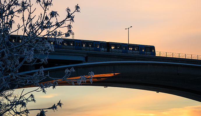 Stockholmsbild. Tunnelbana som åker över en bro i solnedgång.