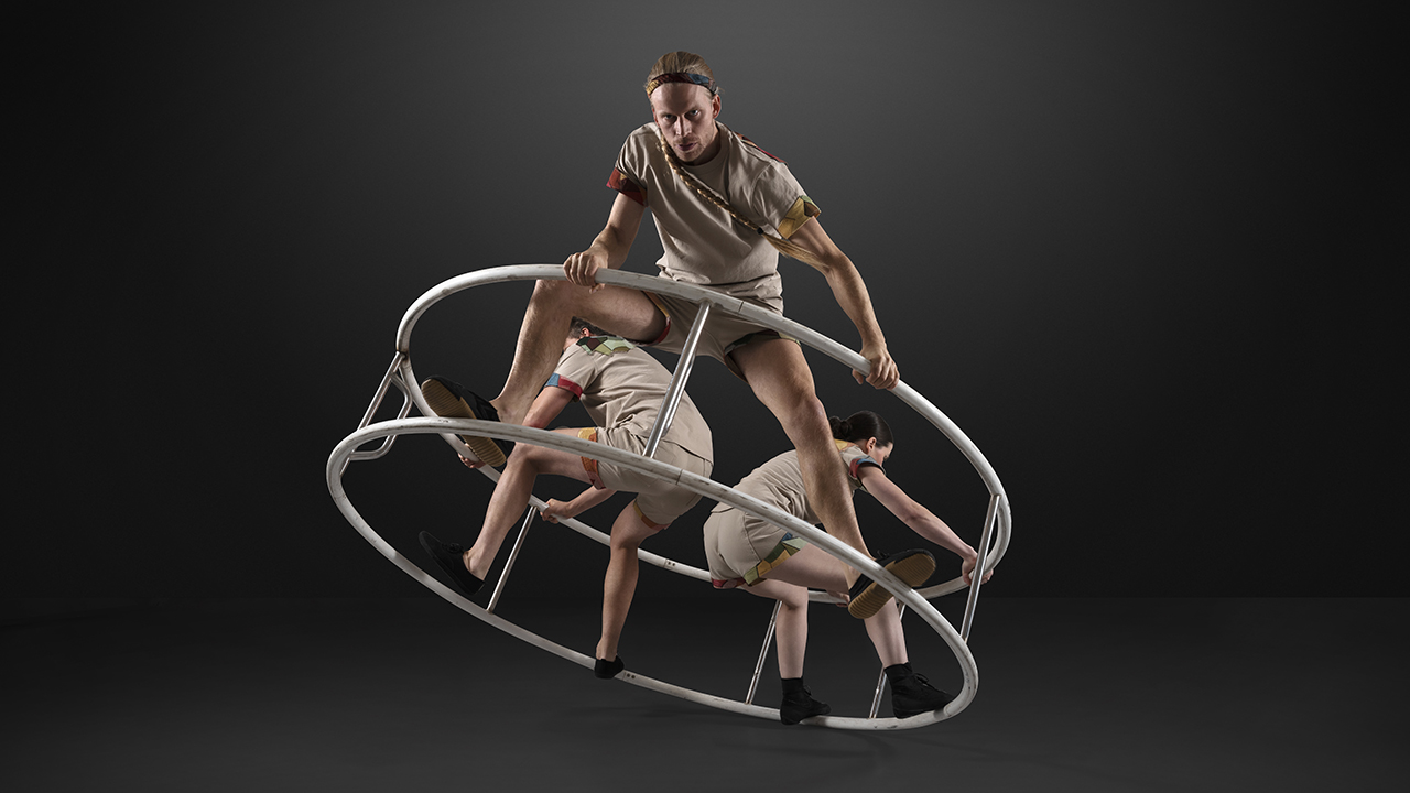 Tre cirkusartister som står inuti en hjulformad ställning