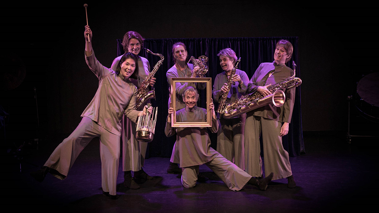 En musikgrupp med sex kvinnor, fem av dem håller i musikinstrument och en håller i en förgylld tavelram