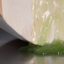 Syntolkning: Närbild av skulpturen Lip Retractor med grön vätska som rinner på en vitlaserat trä