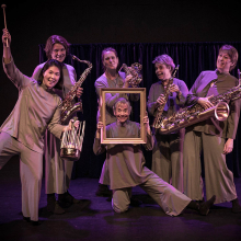 En musikgrupp med sex kvinnor, fem av dem håller i musikinstrument och en håller i en förgylld tavelram