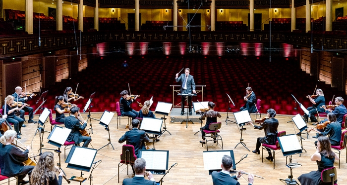 Foto som visar orkestern med en dirigent framför sig. 