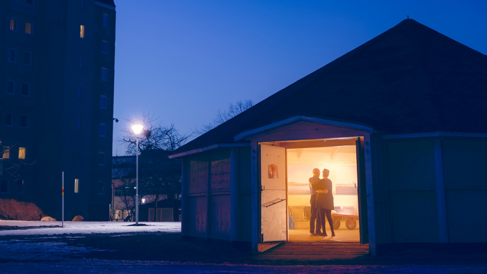 Ett bostadsområde i skymningen, en dörr är öppen till en lokal där det lyser varmt på ett dansande par.